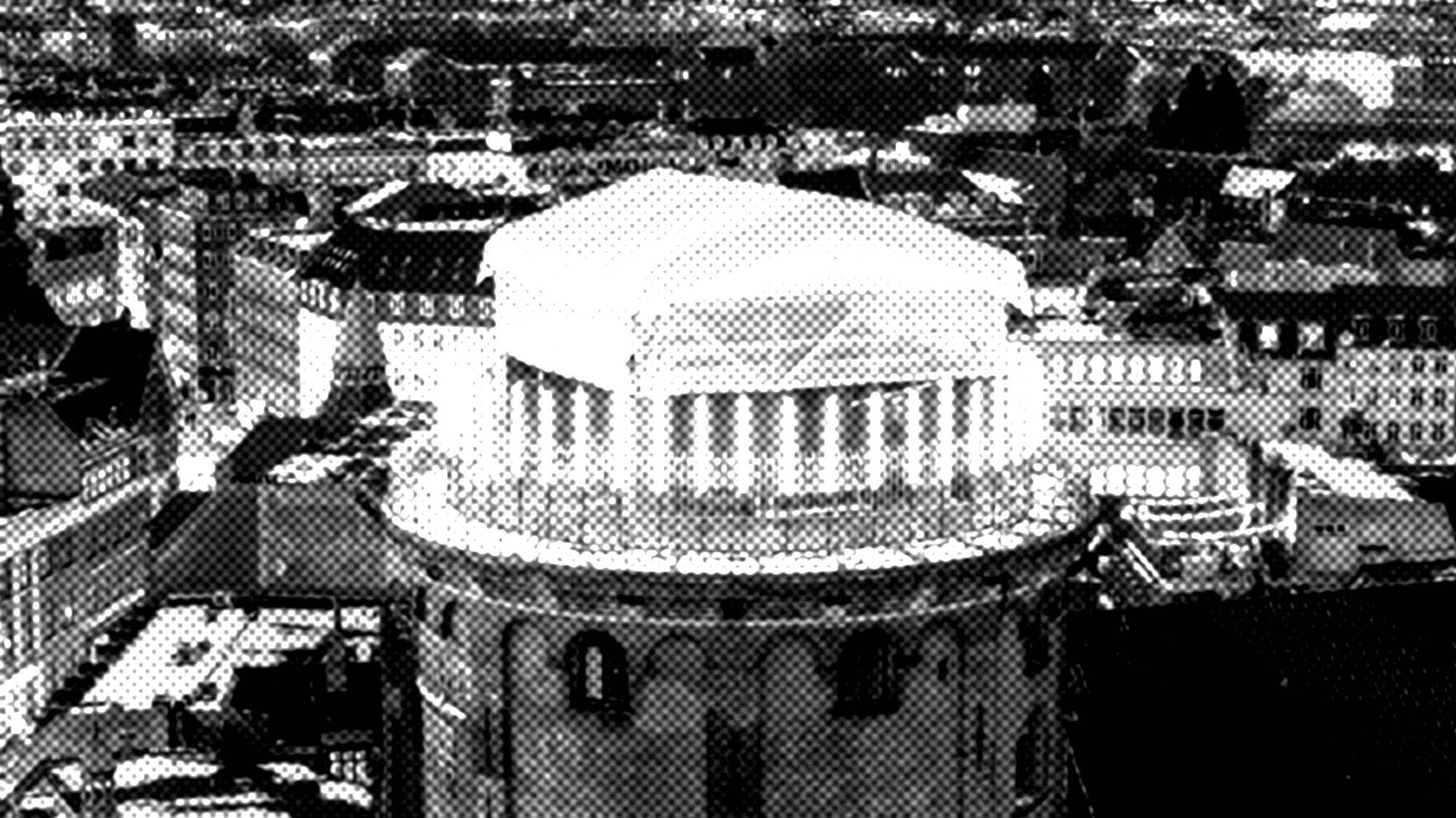 A black-and-white, high-contrast image of a large, round building with columns and a white roof, surrounded by other city buildings.